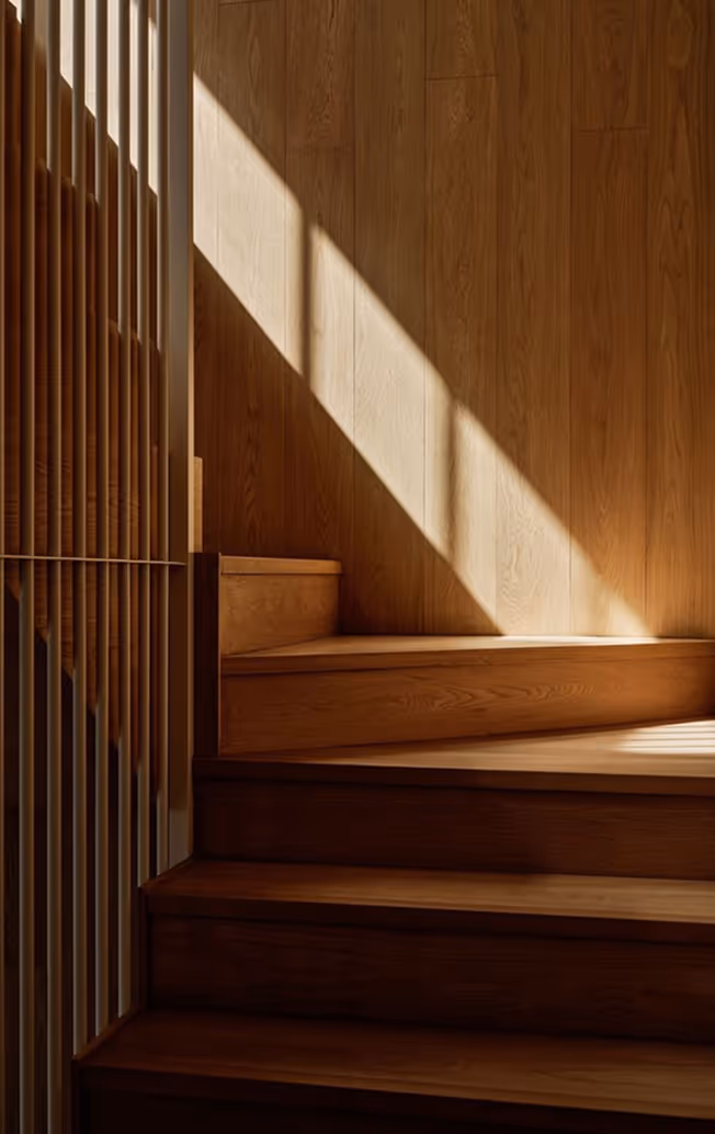 Wooden stairs bathed in sunlight with shadows from vertical slats on the left wall.