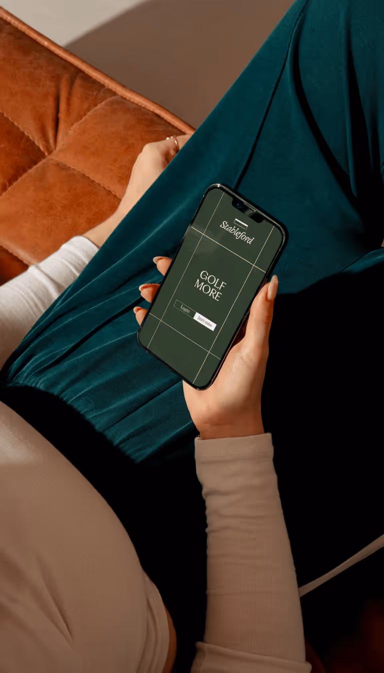 Person holding a smartphone displaying the Stableford app with the text 'GOLF MORE' on the screen.