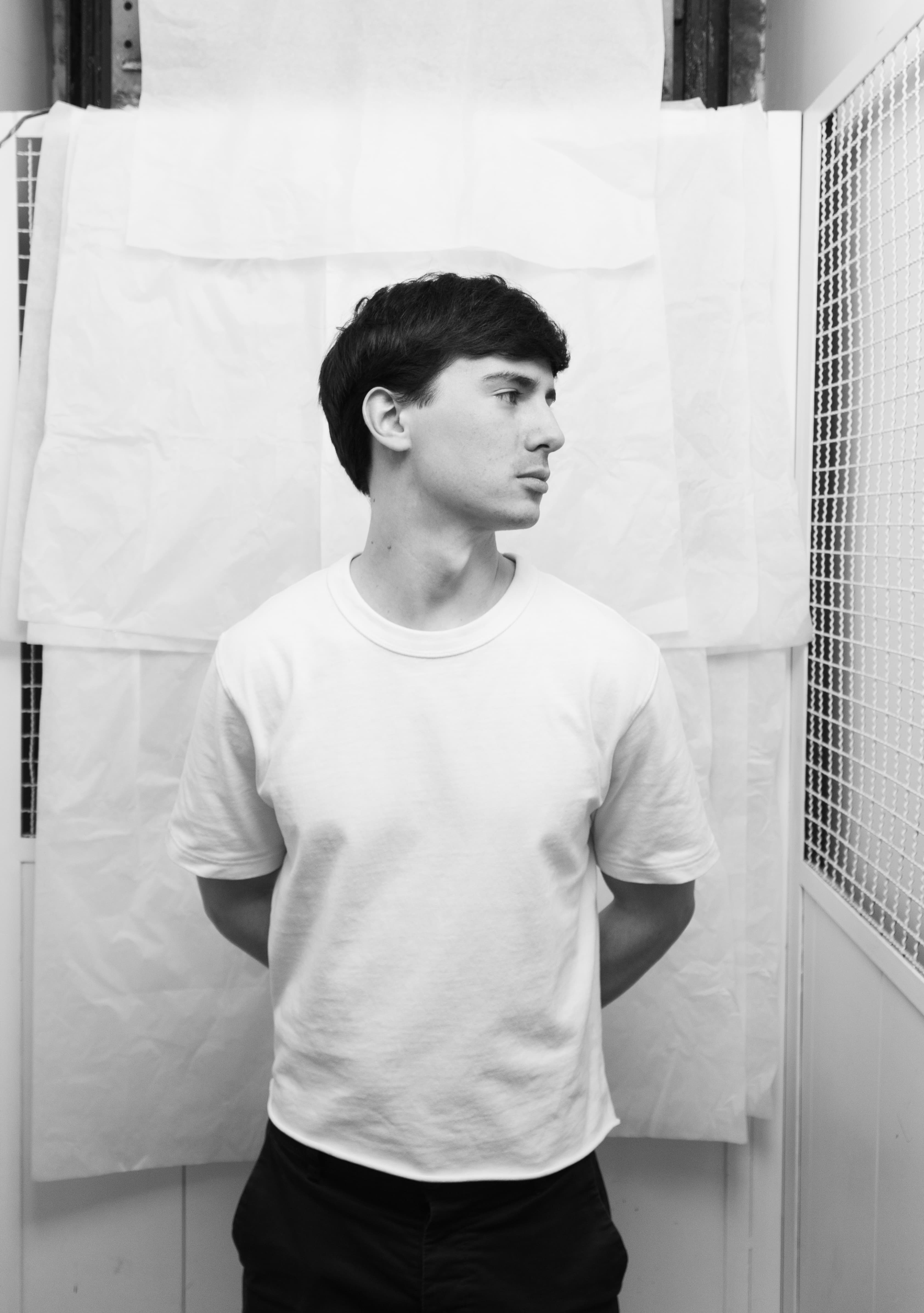 Young man in a white t-shirt looking to the right against a white textured background.