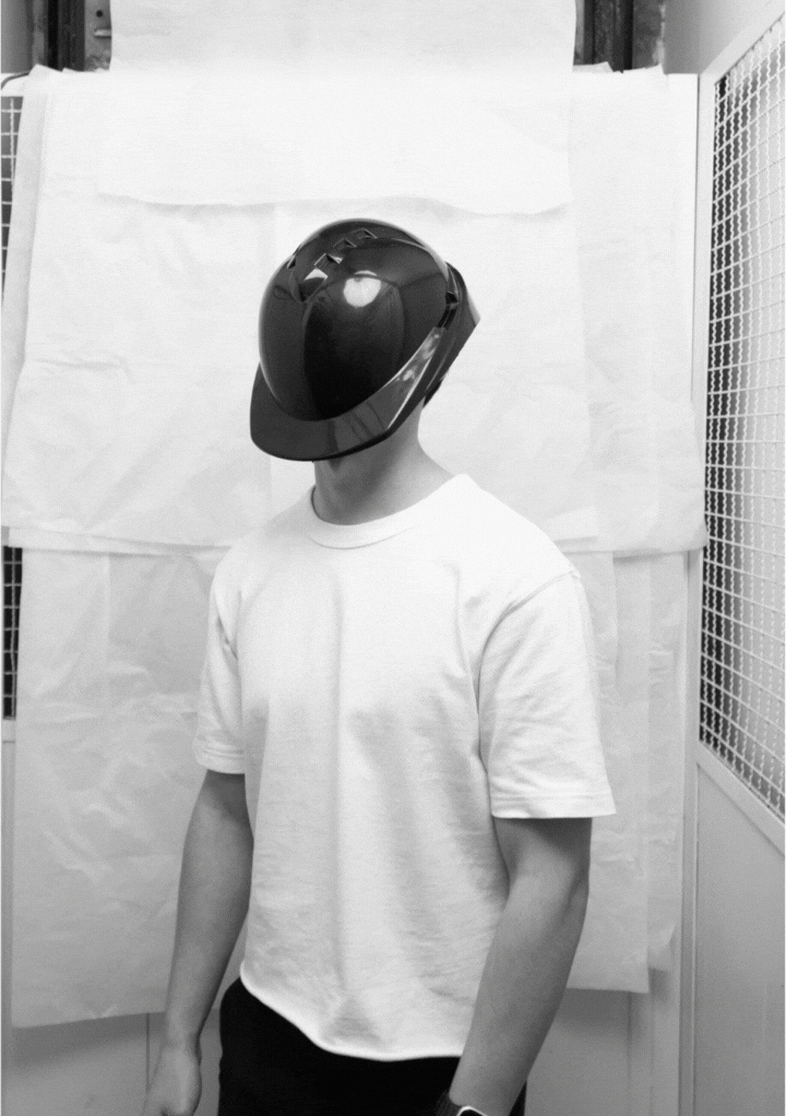Person wearing a black protective hard hat and white t-shirt standing against a plain backdrop.