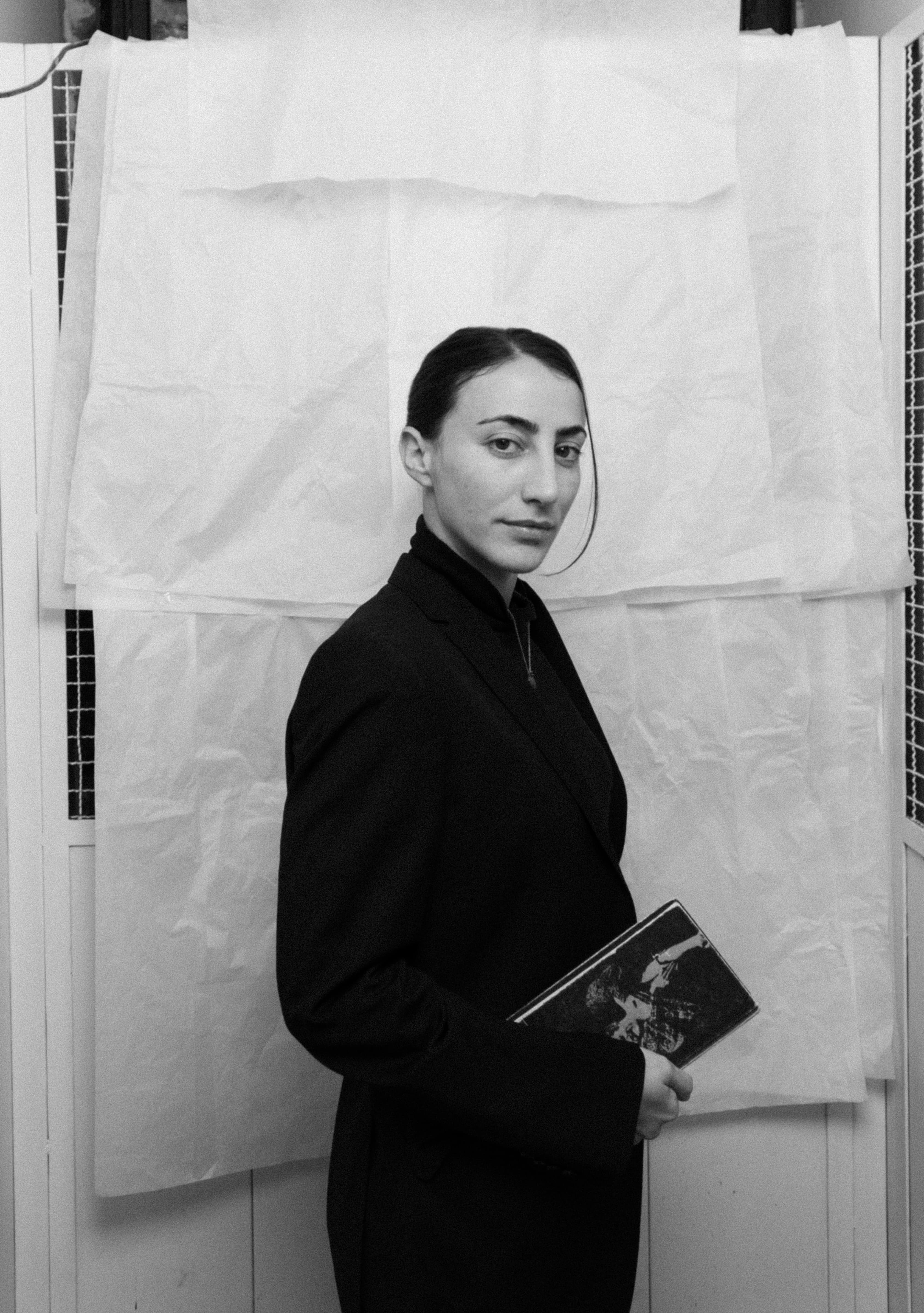 Black and white portrait of a woman in a dark blazer holding a book with an illustrated cover.