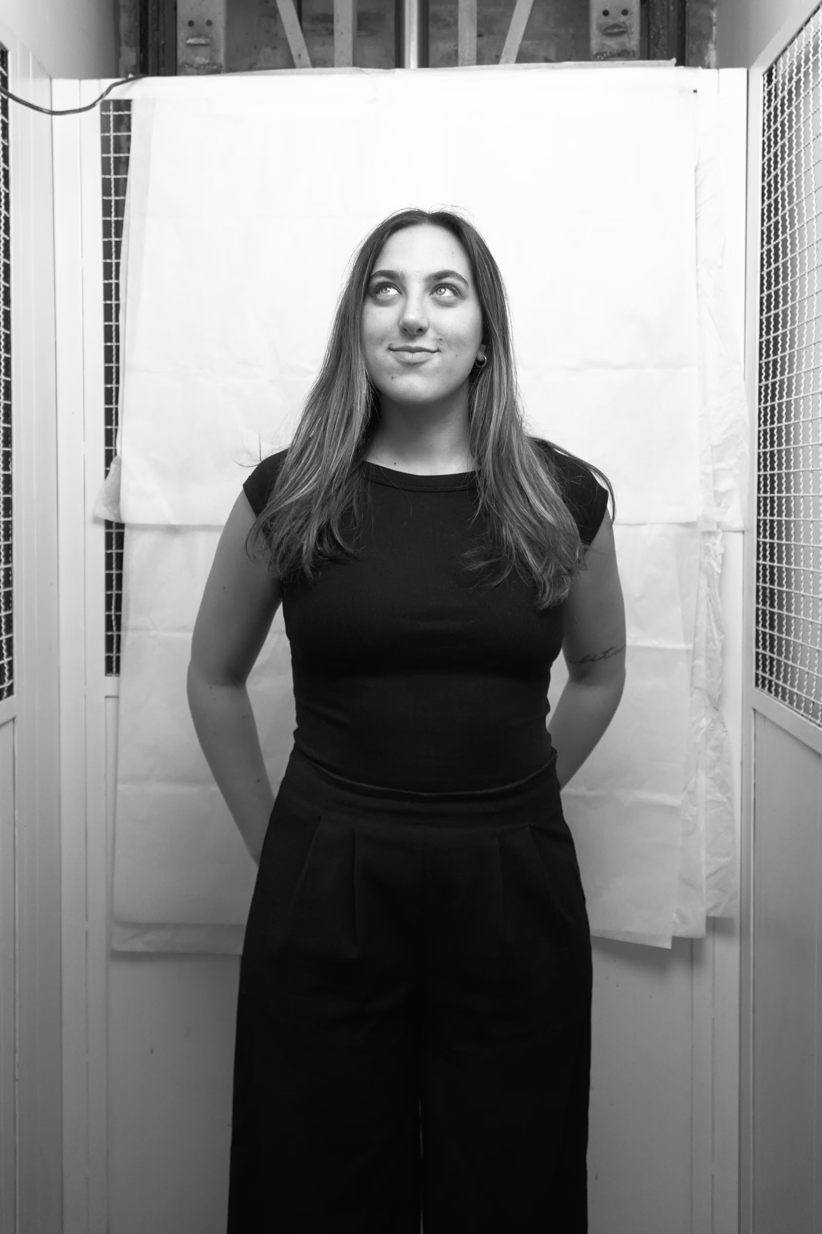 Black and white portrait of a woman with light hair wearing a black long-sleeve top and a heart-shaped pendant, looking to the side.