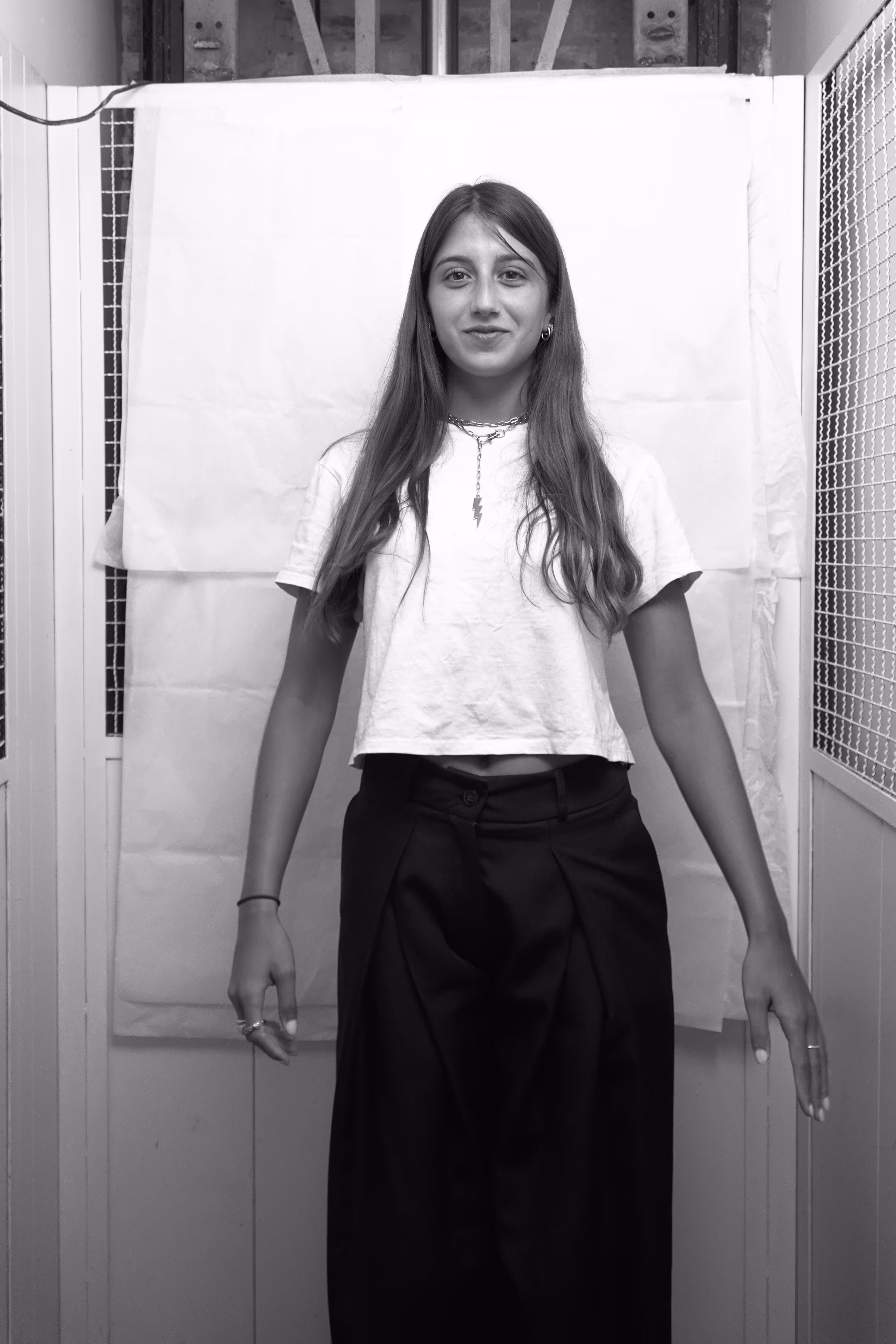 Black and white portrait of a woman with light hair wearing a black long-sleeve top and a heart-shaped pendant, looking to the side.