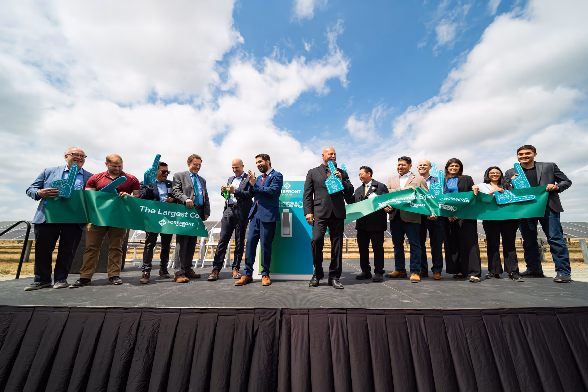 Group cutting a green ribbon at an outdoor solar energy event under a partly cloudy sky.