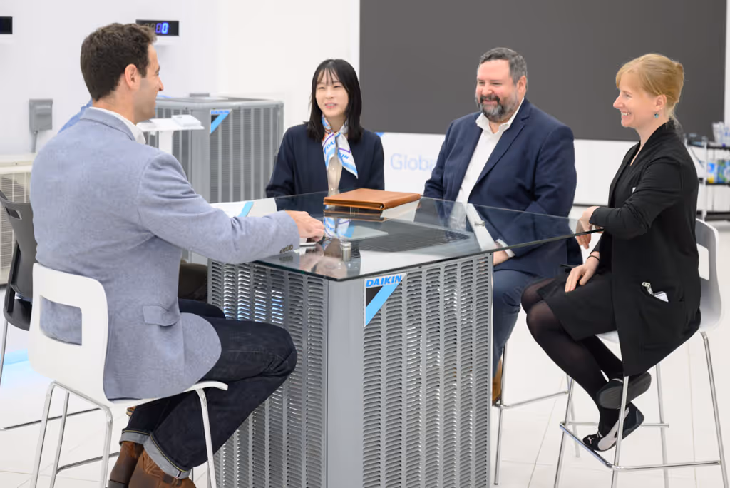 Four people sitting around a glass table with a Daikin air conditioning unit base, smiling and conversing.