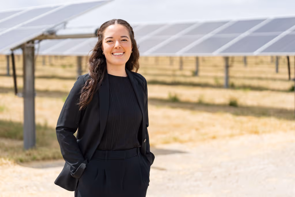 Smiling woman in black suit standing in front of solar panels in a sunny field.