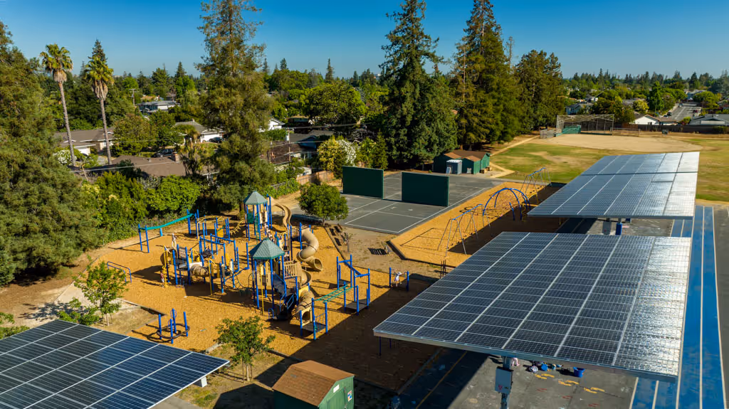 Playground with slides and swings beside solar panel canopies and tennis courts in a park area.