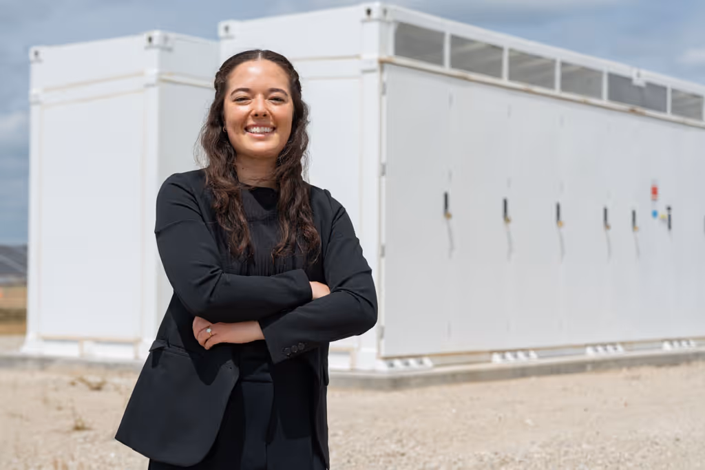 Smiling woman in black business attire with arms crossed standing in front of white industrial containers.