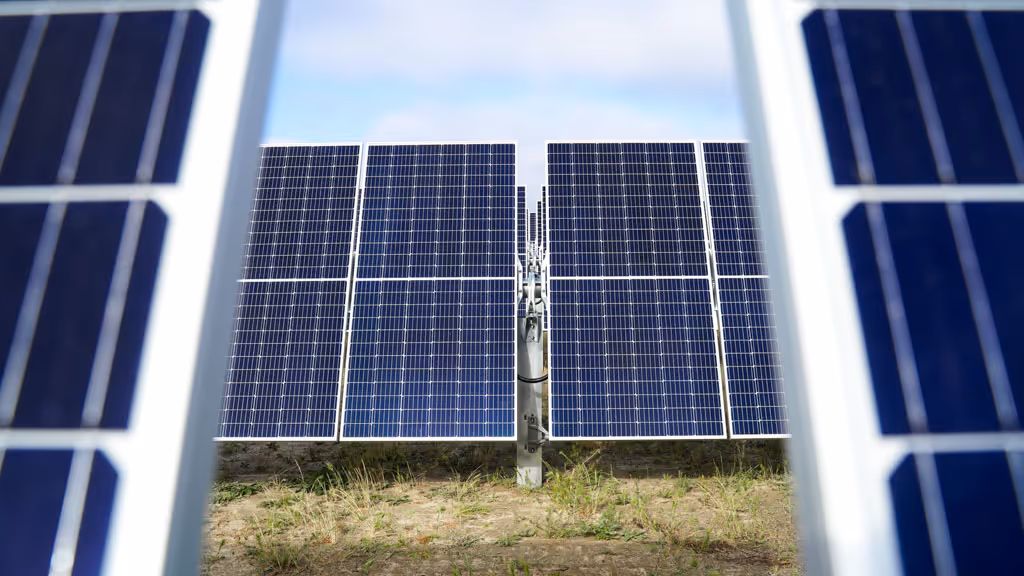 Rows of solar panels installed on a grassy field under a partly cloudy sky.