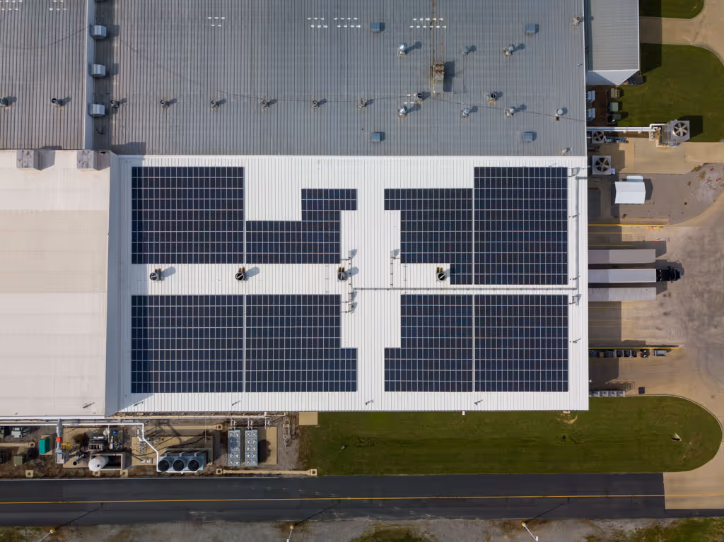 Aerial view of large white industrial building rooftop with multiple dark solar panels installed.