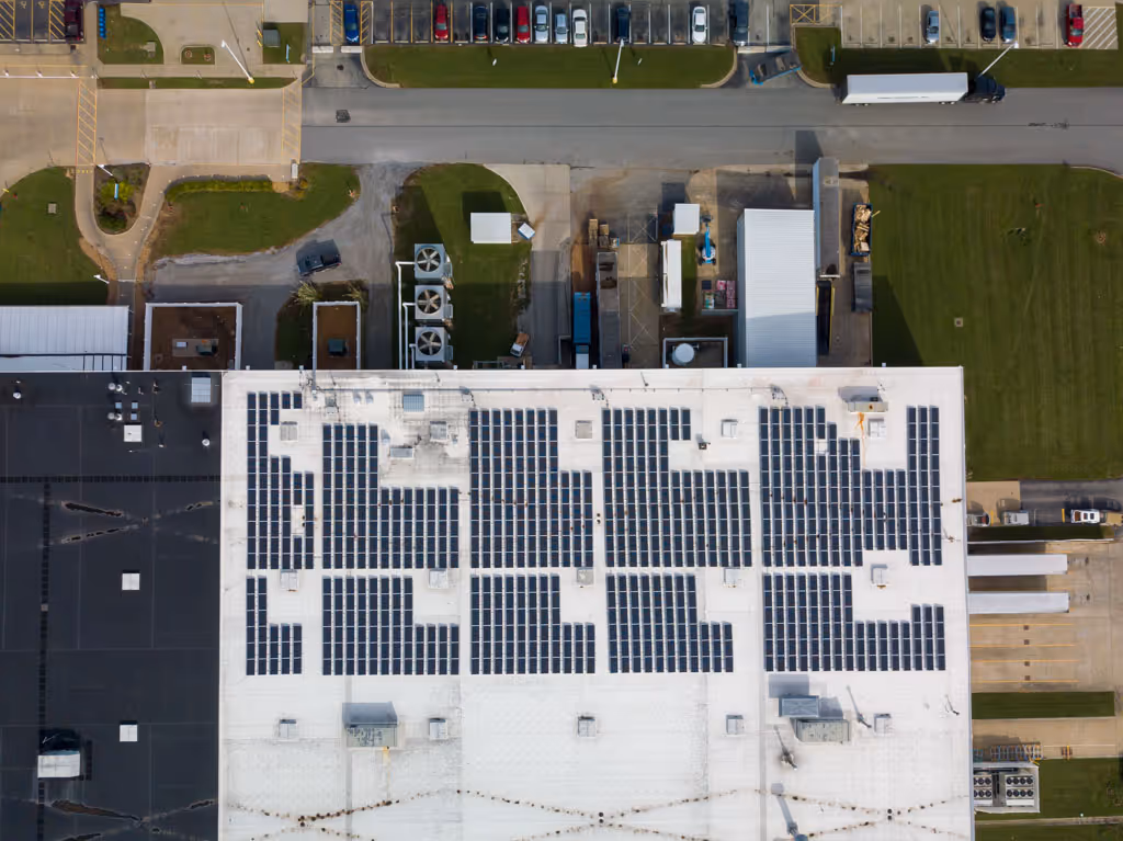Aerial view of a large white commercial building with dark solar panels installed on its flat roof.