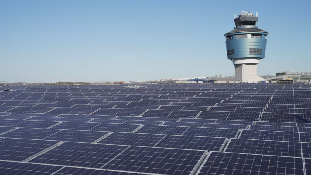 Large array of solar panels on a rooftop with an airport control tower in the background.