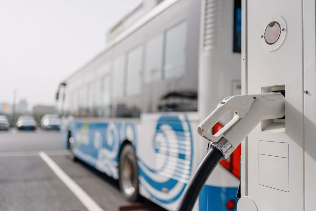 Electric charging plug connected to a station with a bus in the blurred background.