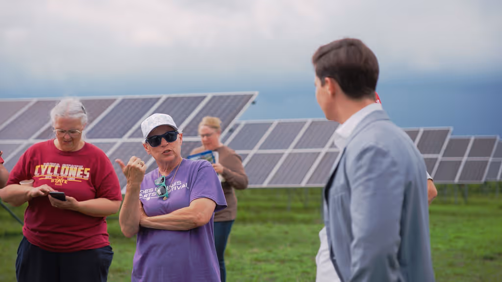 Group of people standing near solar panels outdoors with one person talking and gesturing.