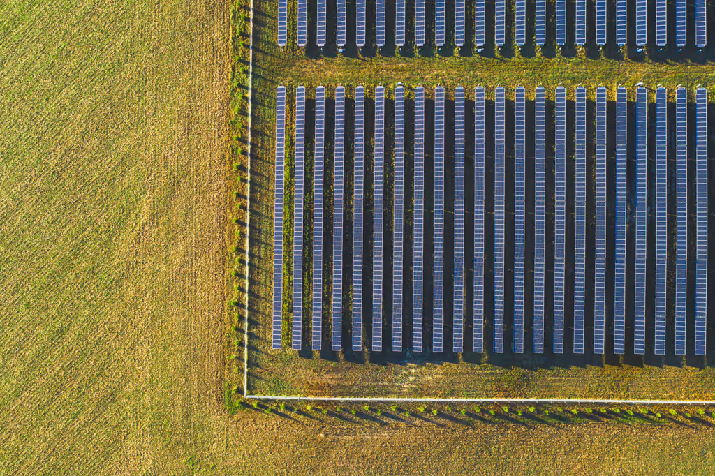 Aerial view of solar panels arranged in rows on green grass land next to a fenced field.