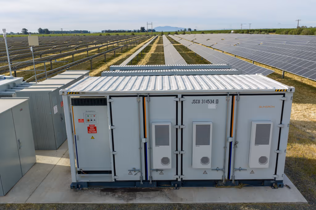 Large battery storage unit at solar farm with rows of solar panels in the background.