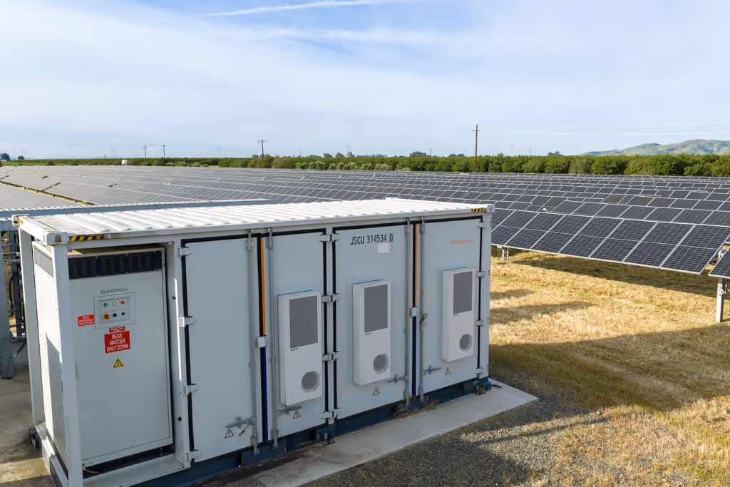 Large battery storage unit near an expansive field of solar panels under a clear sky.