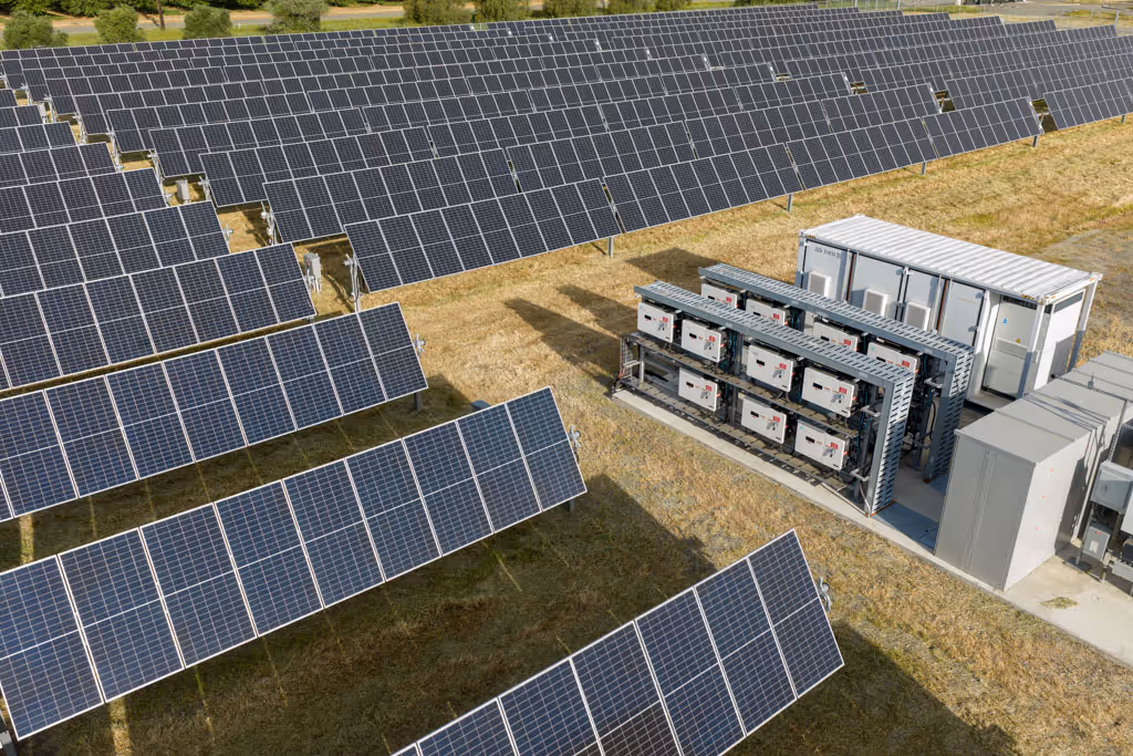 Rows of solar panels next to battery storage units in a solar power facility on grass.
