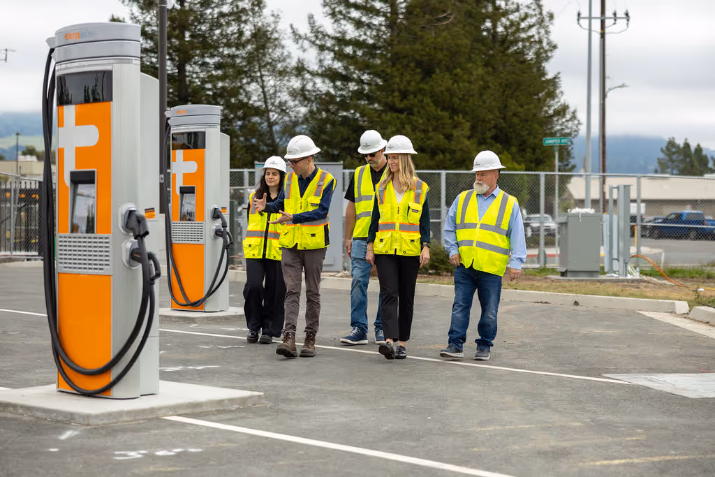 Five workers in hard hats and safety vests inspecting electric vehicle charging stations outdoors.