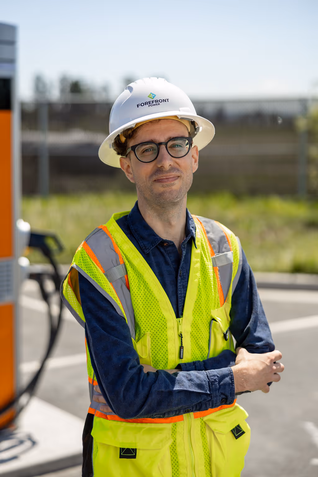 Man wearing Forefront Power helmet and neon safety vest with crossed arms outdoors.