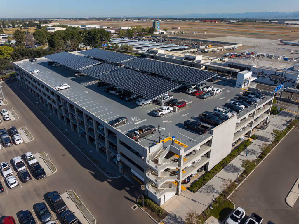 Aerial view of a multi-level parking garage with solar panels on the roof beside an airport runway.