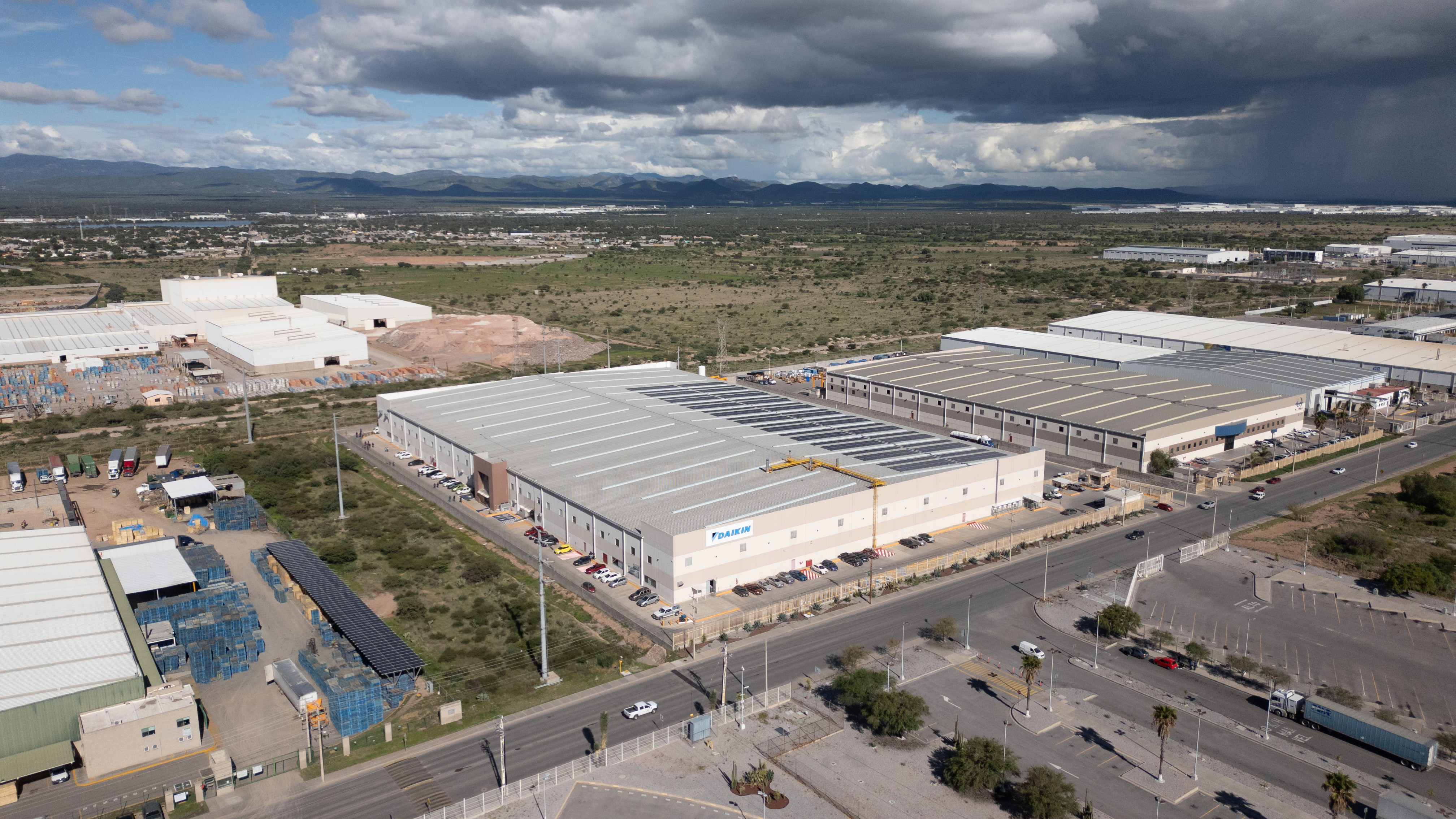 Aerial view of Daikin industrial warehouse with parked cars along the roadside under a cloudy sky.