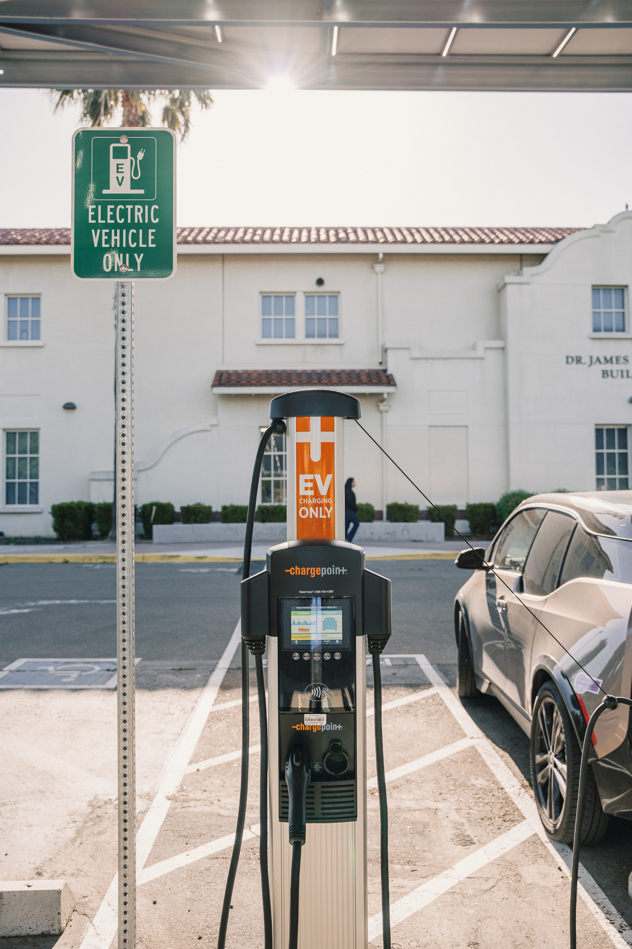 Electric vehicle charging station with a plugged-in car and a green Electric Vehicle Only sign nearby.
