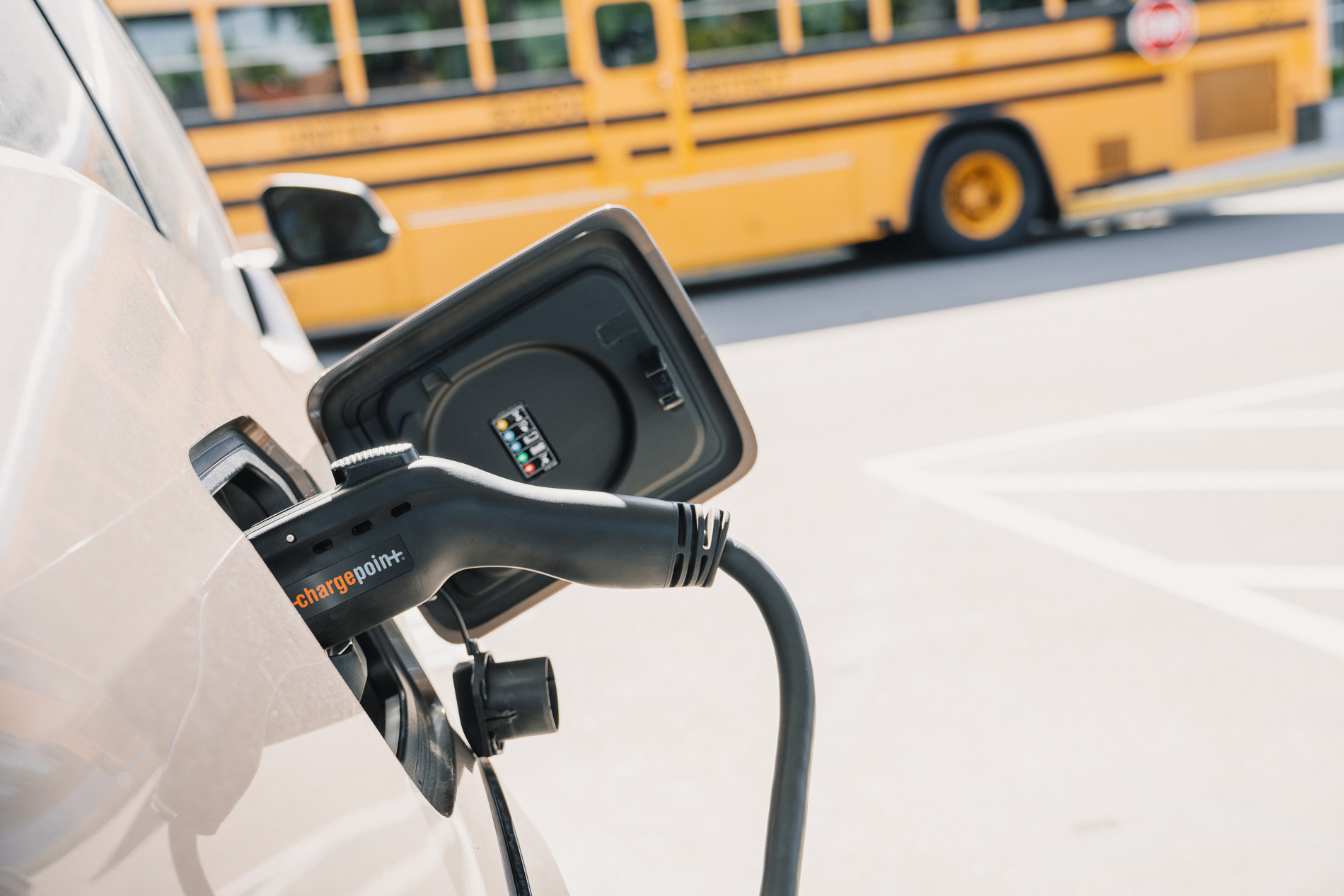 Electric vehicle charging with a ChargePoint plug connected, yellow school bus in the background.
