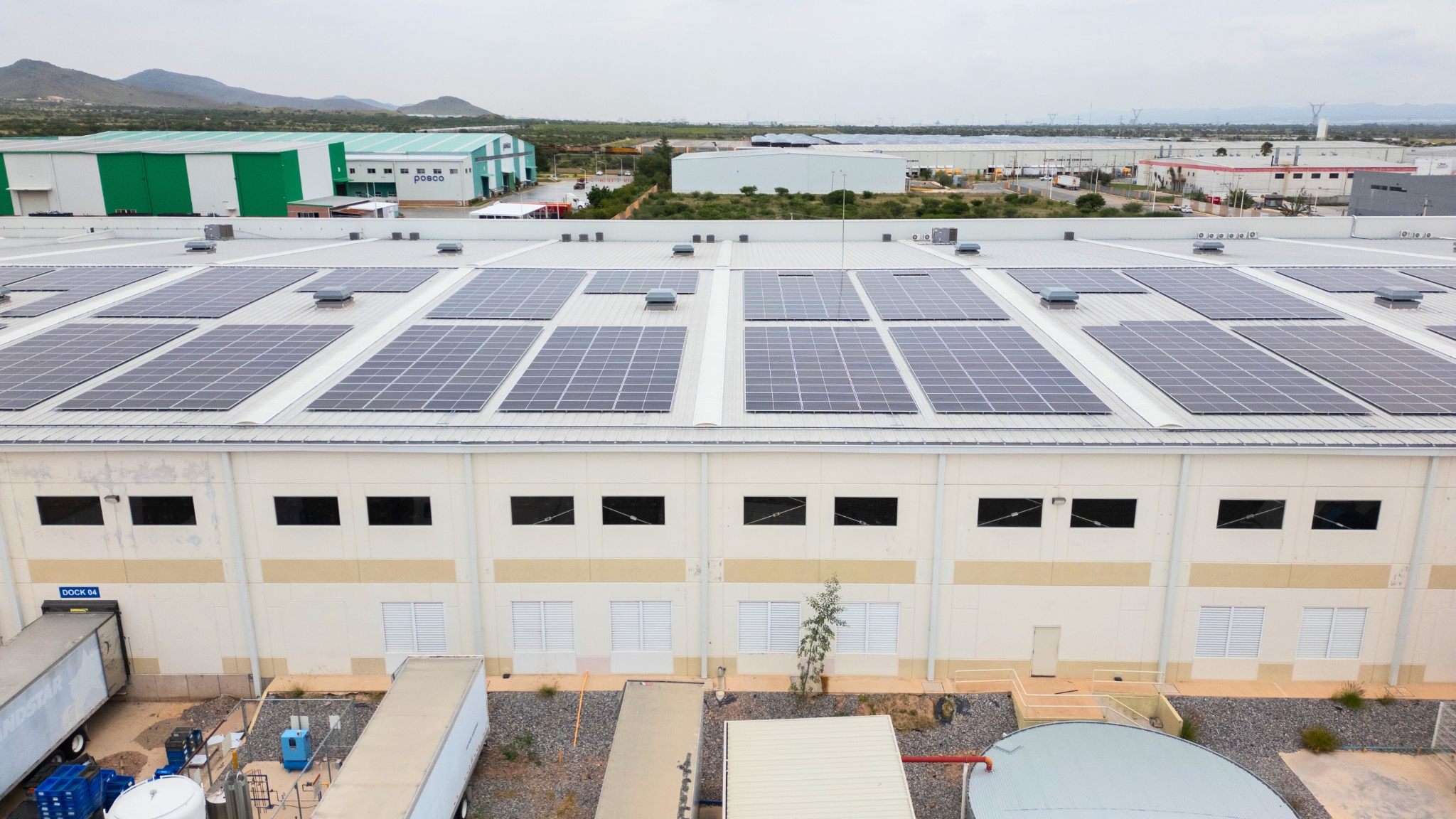 Industrial warehouse roof covered with solar panels and trucks parked alongside the building.