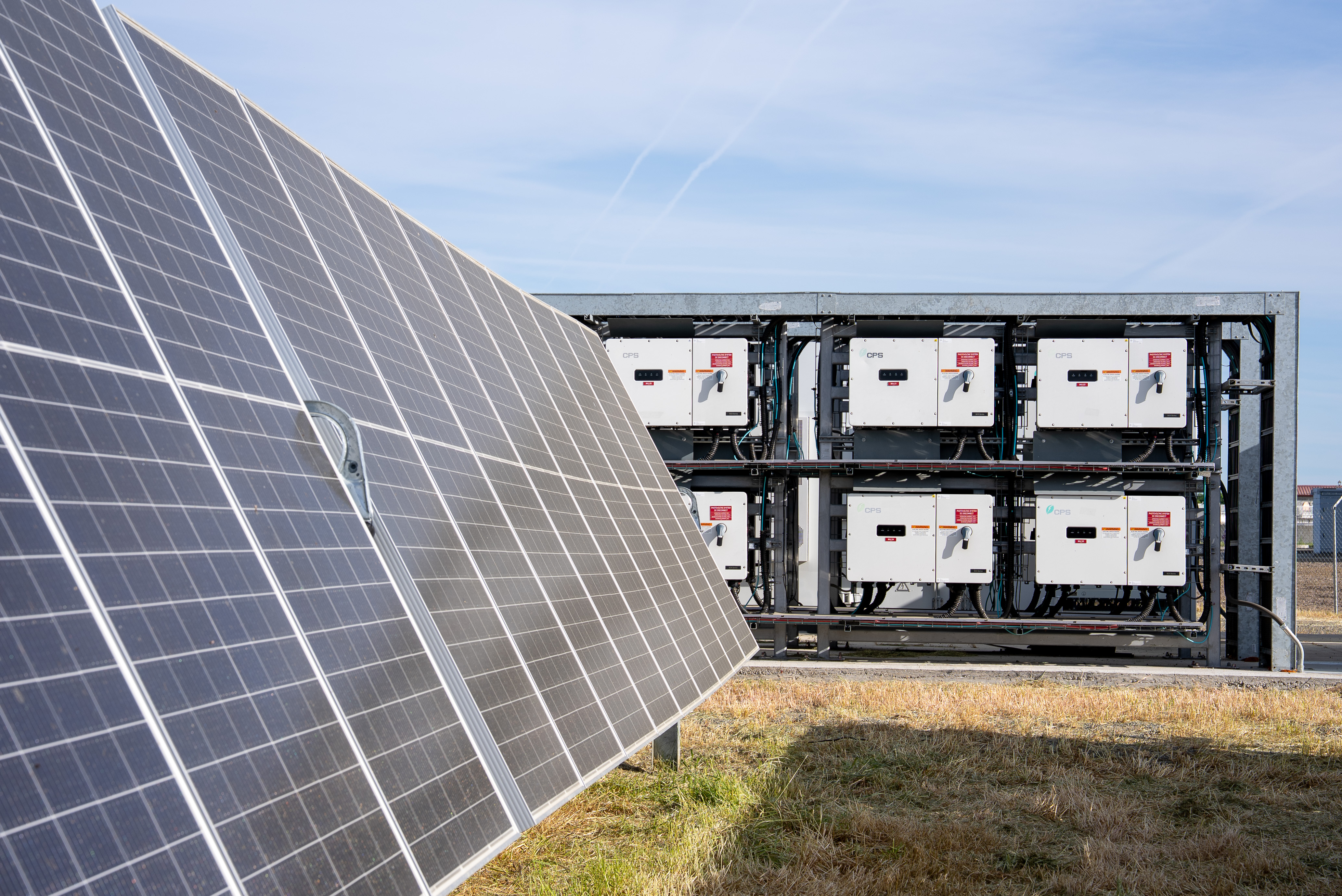 Solar panels angled on the left with electrical control units mounted on a metal frame on the right outdoors.