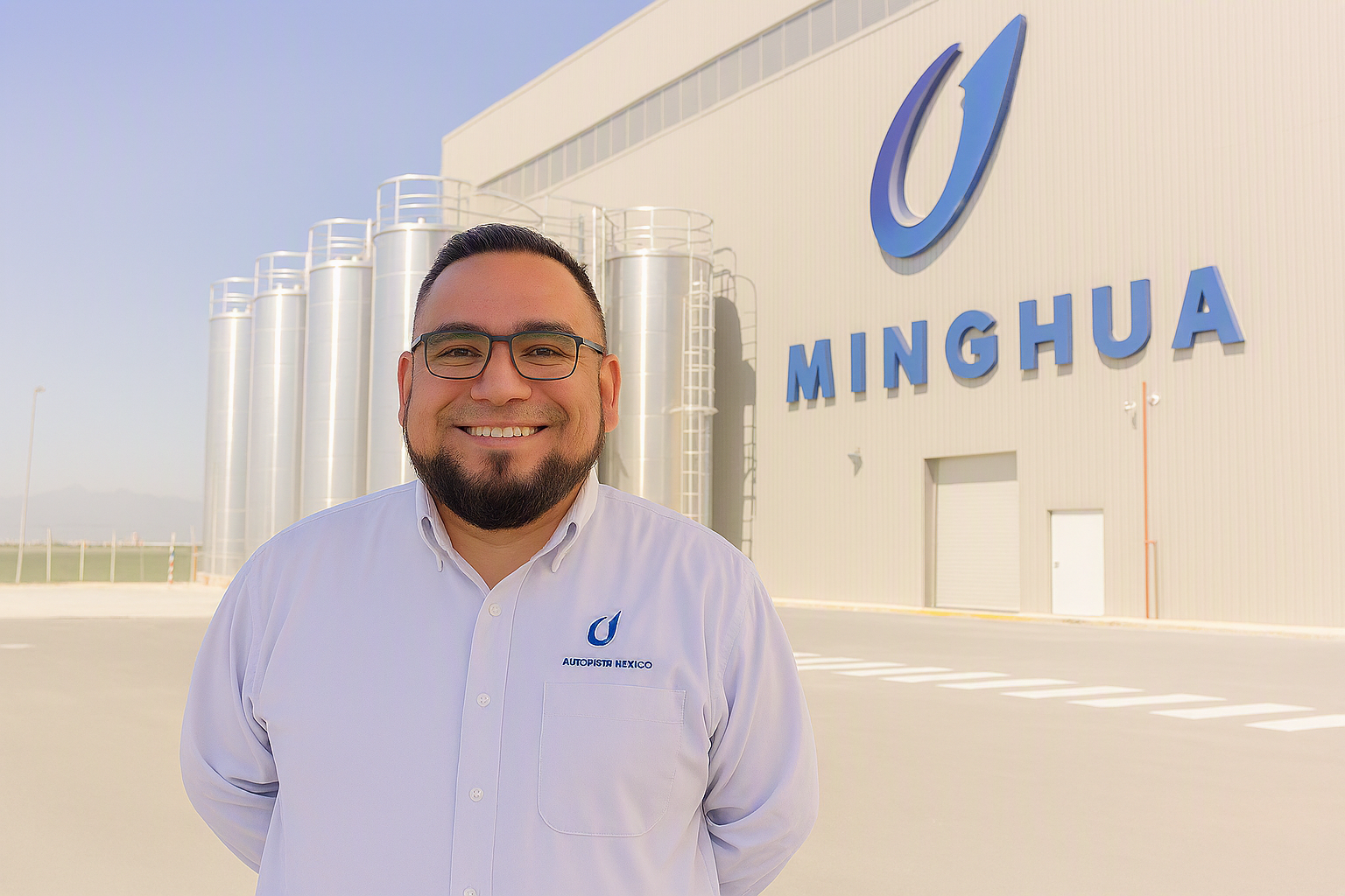 Smiling man with glasses in white shirt standing outside a building with MINGHUA sign and silos.