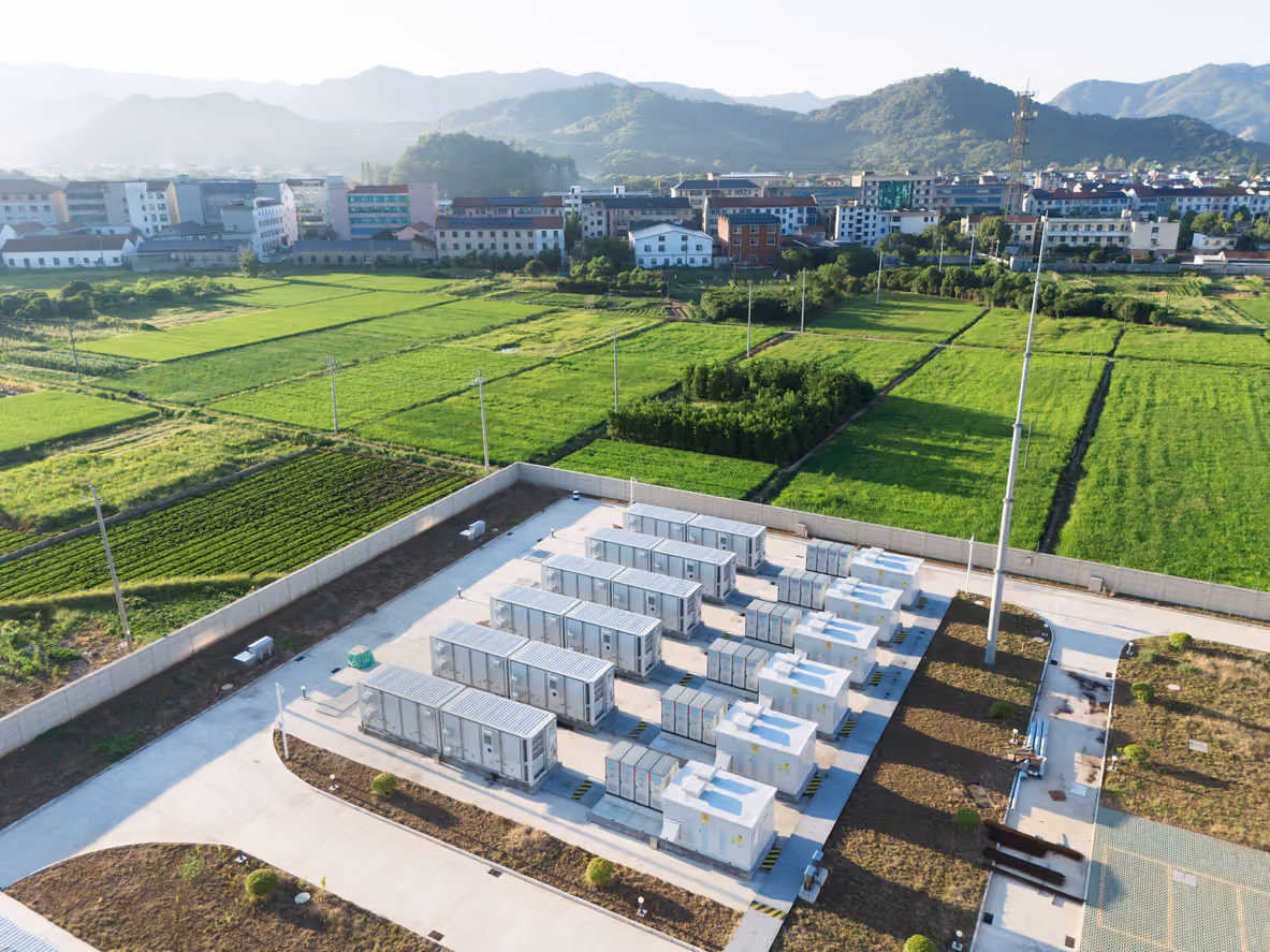 Aerial view of a solar power station with multiple inverter units surrounded by green fields near a town.