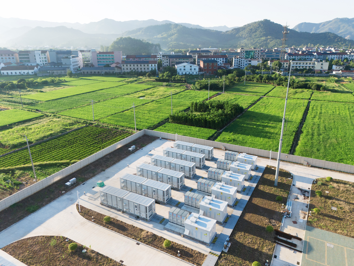 Aerial view of a solar power station with multiple inverter units surrounded by green fields near a town.