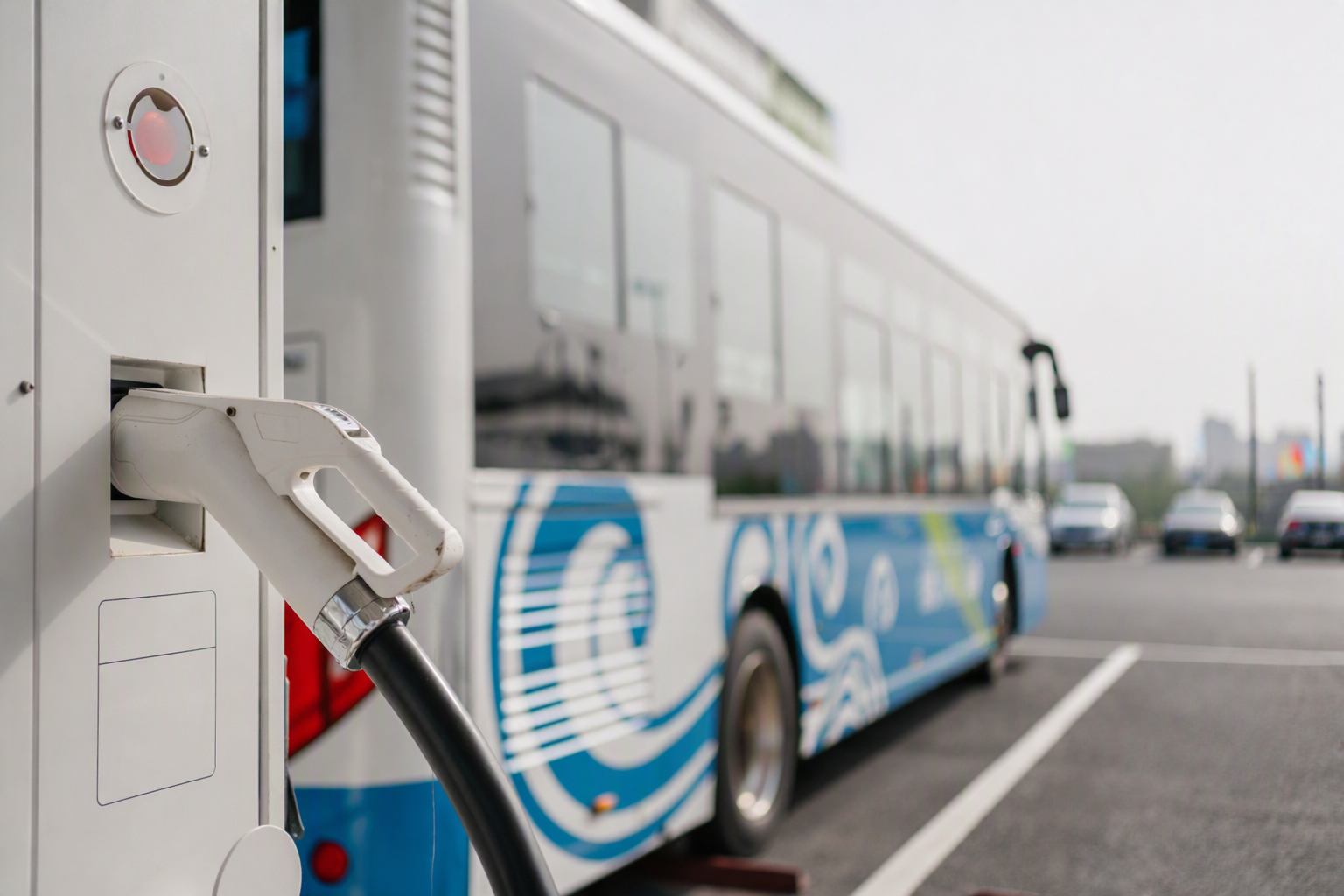 Electric bus plugged into a white charging station in a parking lot.
