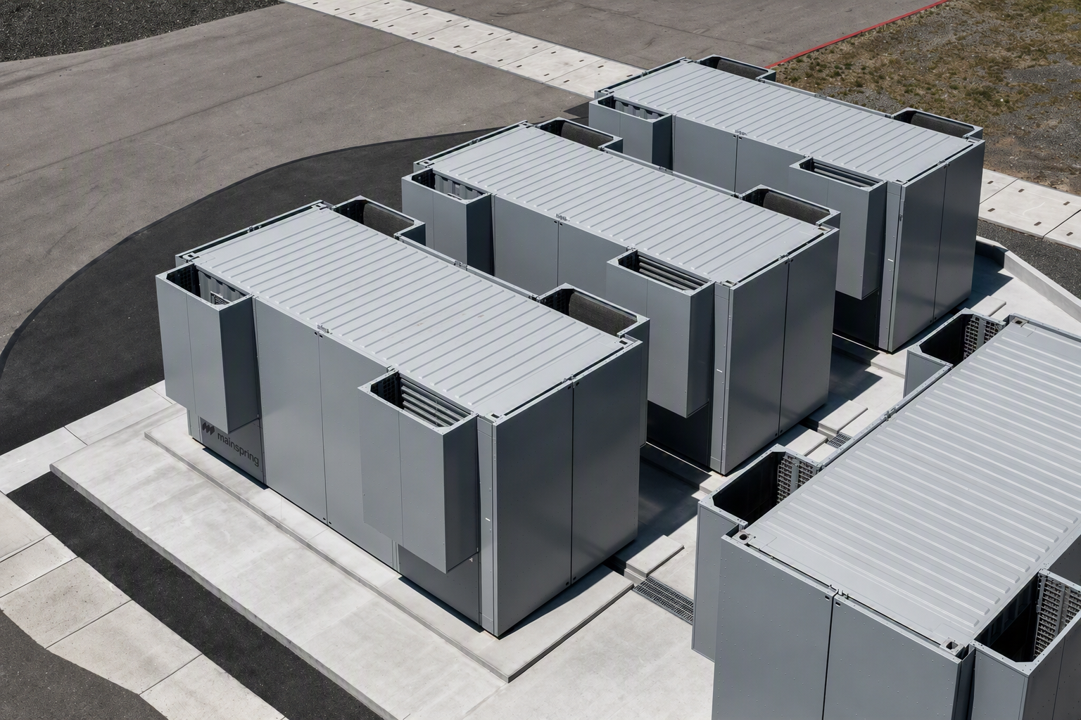 Aerial view of four large, rectangular gray industrial units on a concrete platform outdoors.