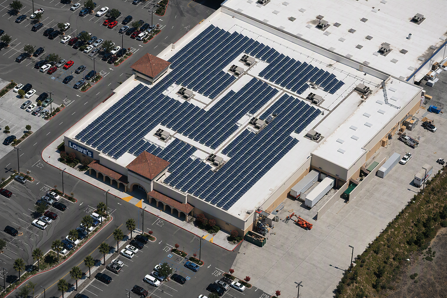Aerial view of a Lowe's store roof covered with solar panels and surrounding parking lot.