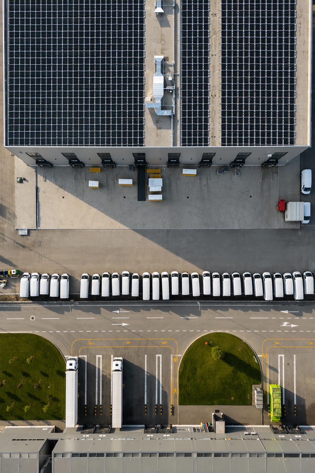 Aerial view of warehouse with solar panels on roof and multiple white trucks parked outside.