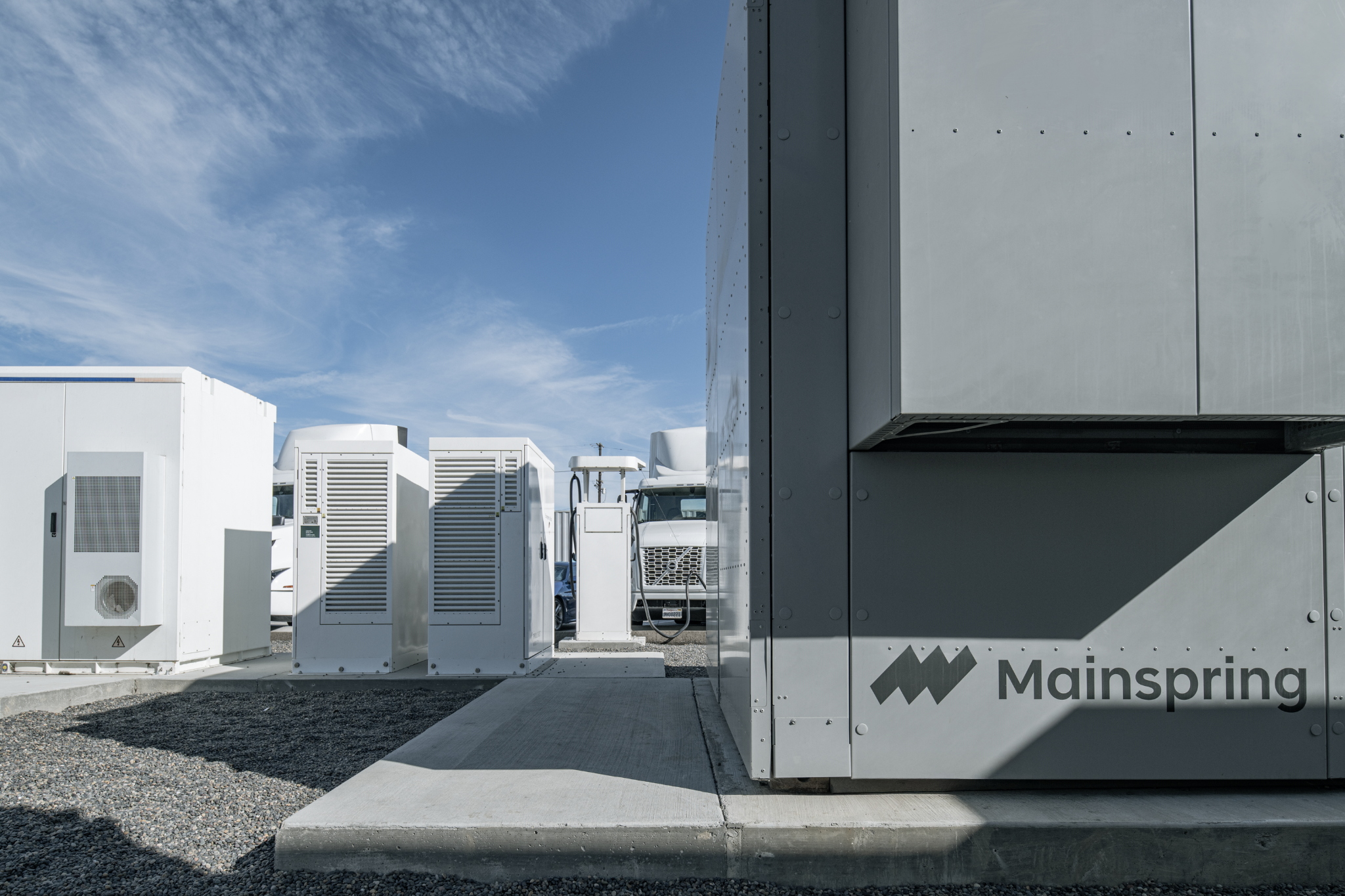 Outdoor energy storage units with Mainspring logo under blue sky and clouds.