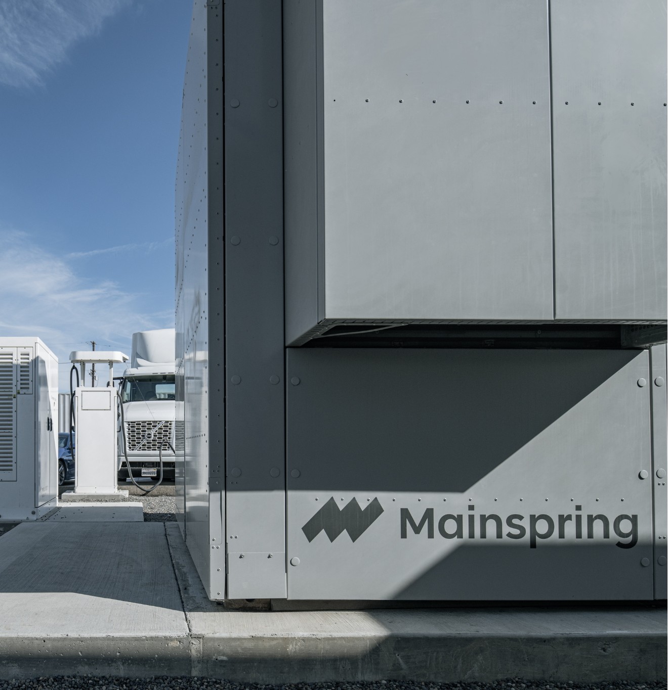 White electric truck at a charging station next to a large gray Mainspring energy storage unit.
