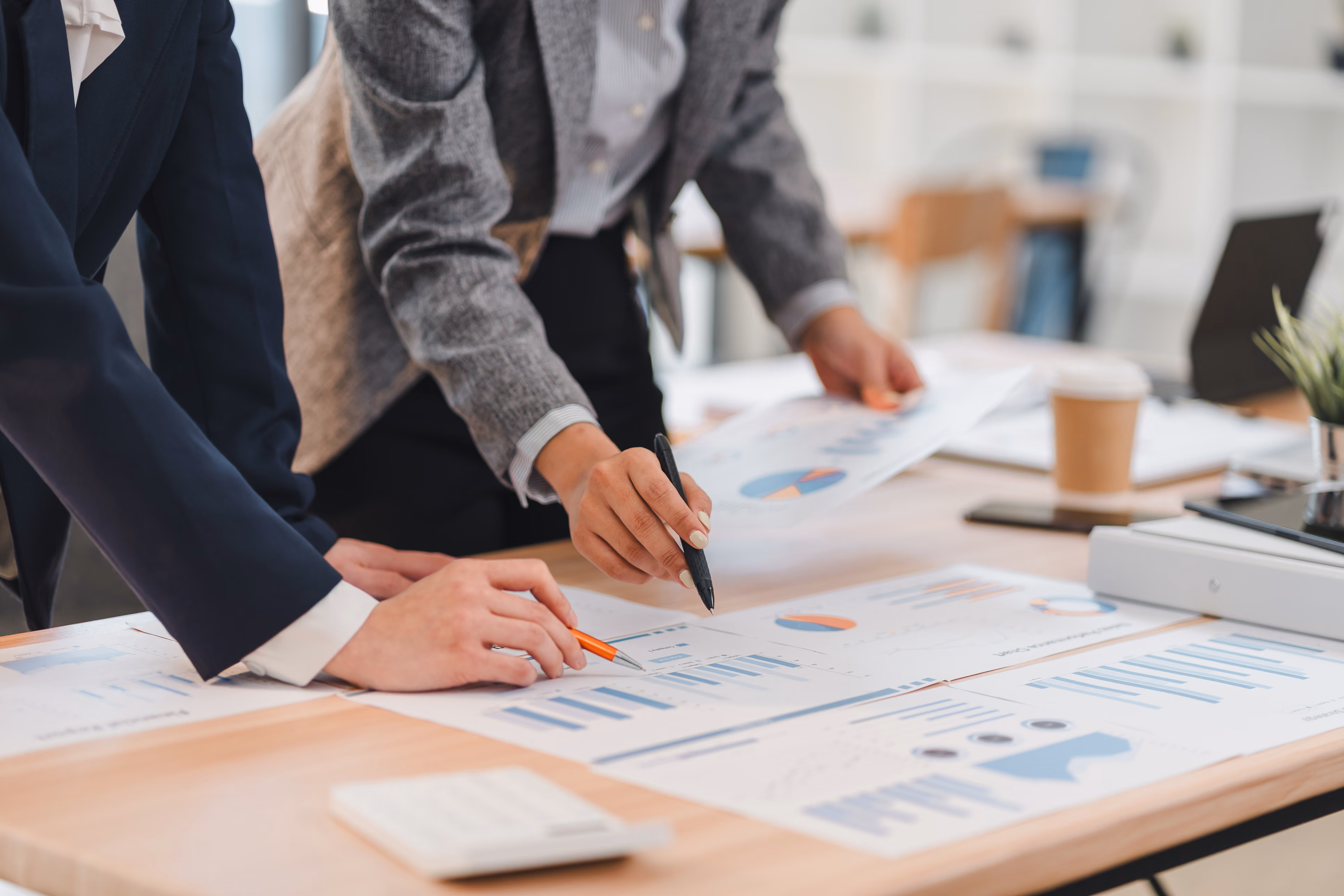 Two business professionals analyze printed charts and graphs spread out on a desk in an office.