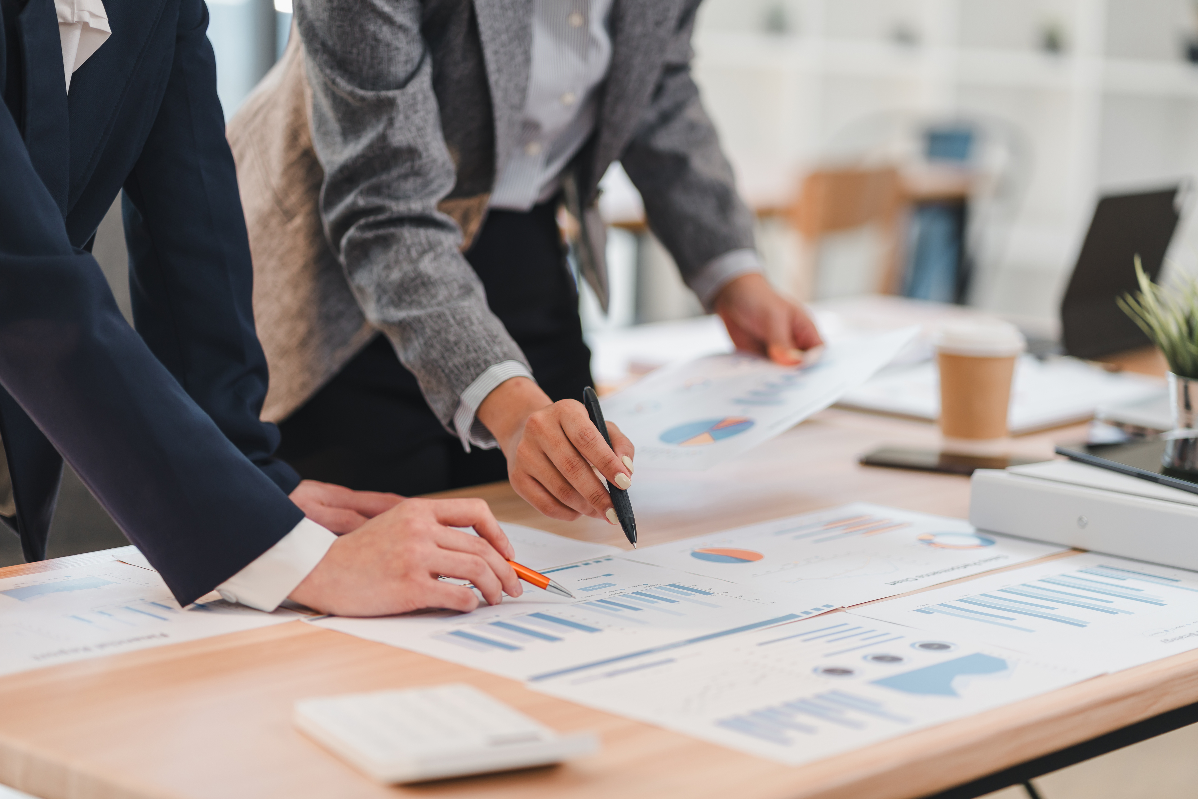 Two business professionals analyze printed charts and graphs spread out on a desk in an office.