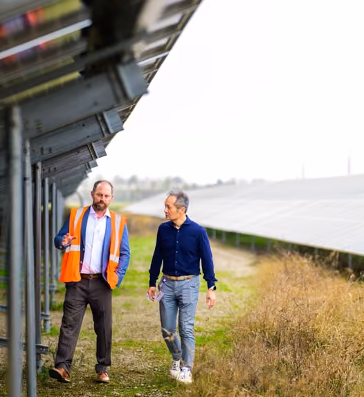 Two men walking and talking under solar panels in an outdoor solar farm.