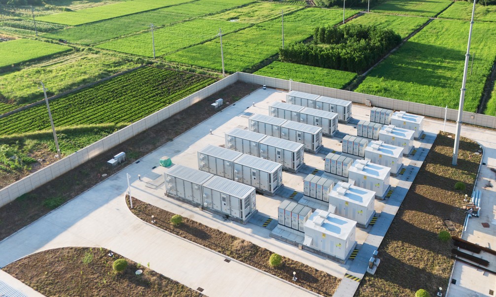 Aerial view of an outdoor electrical substation surrounded by green agricultural fields.