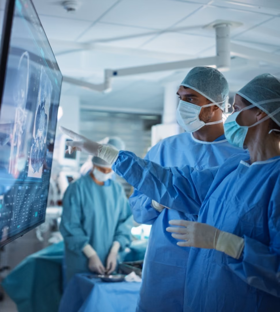 Two surgeons in blue scrubs and masks reviewing brain scans on a large monitor during surgery.