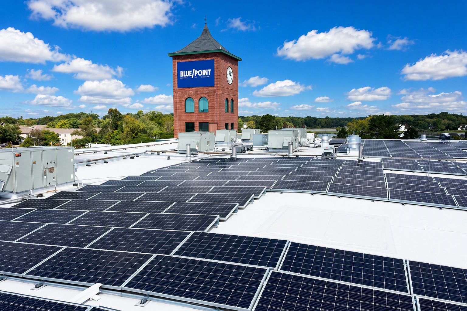 Rooftop solar panels with a brick tower labeled Blue Point Brewing under a bright blue sky with clouds.