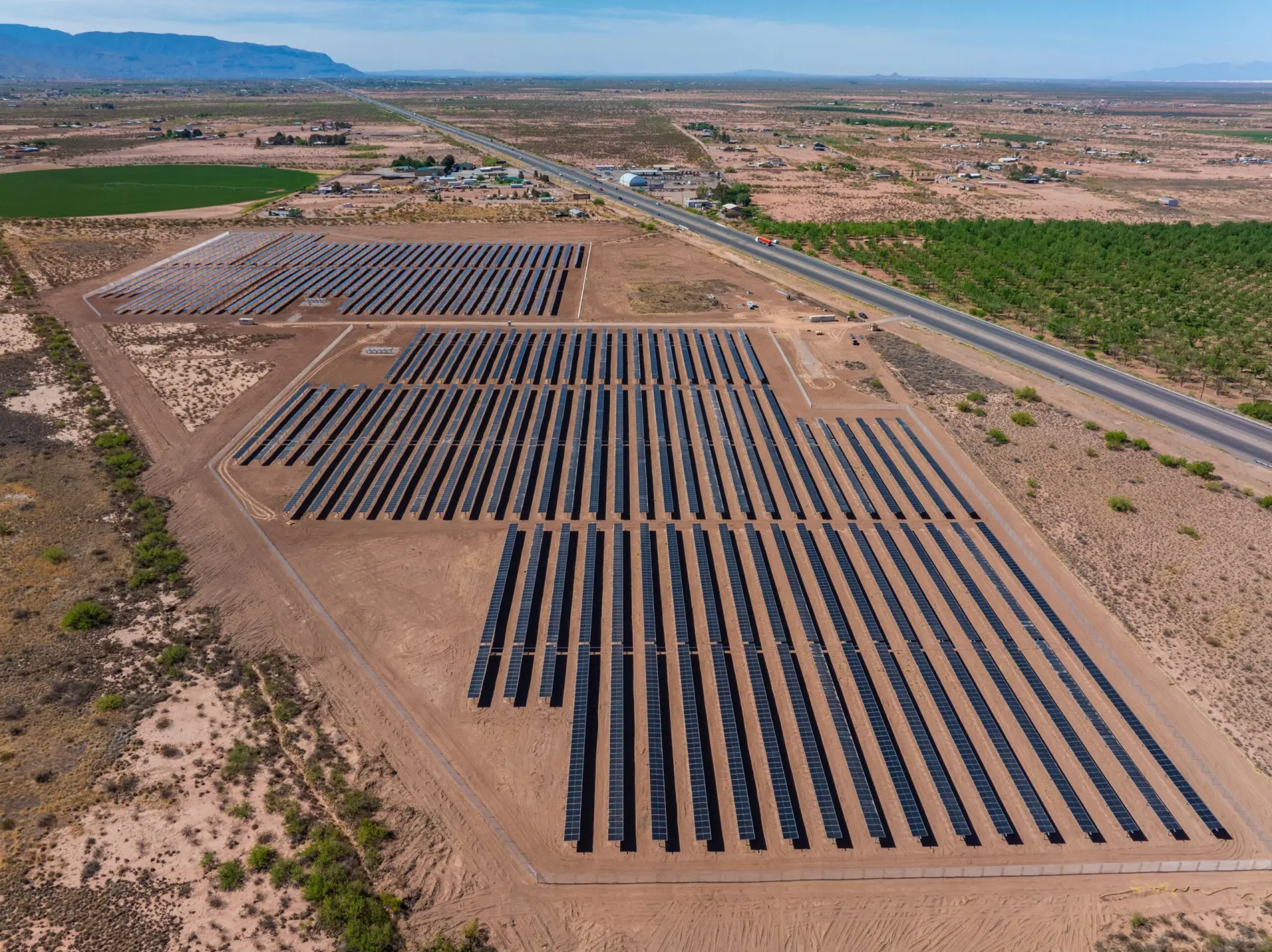 Large solar farm with rows of solar panels in a desert landscape near a road and distant mountains.