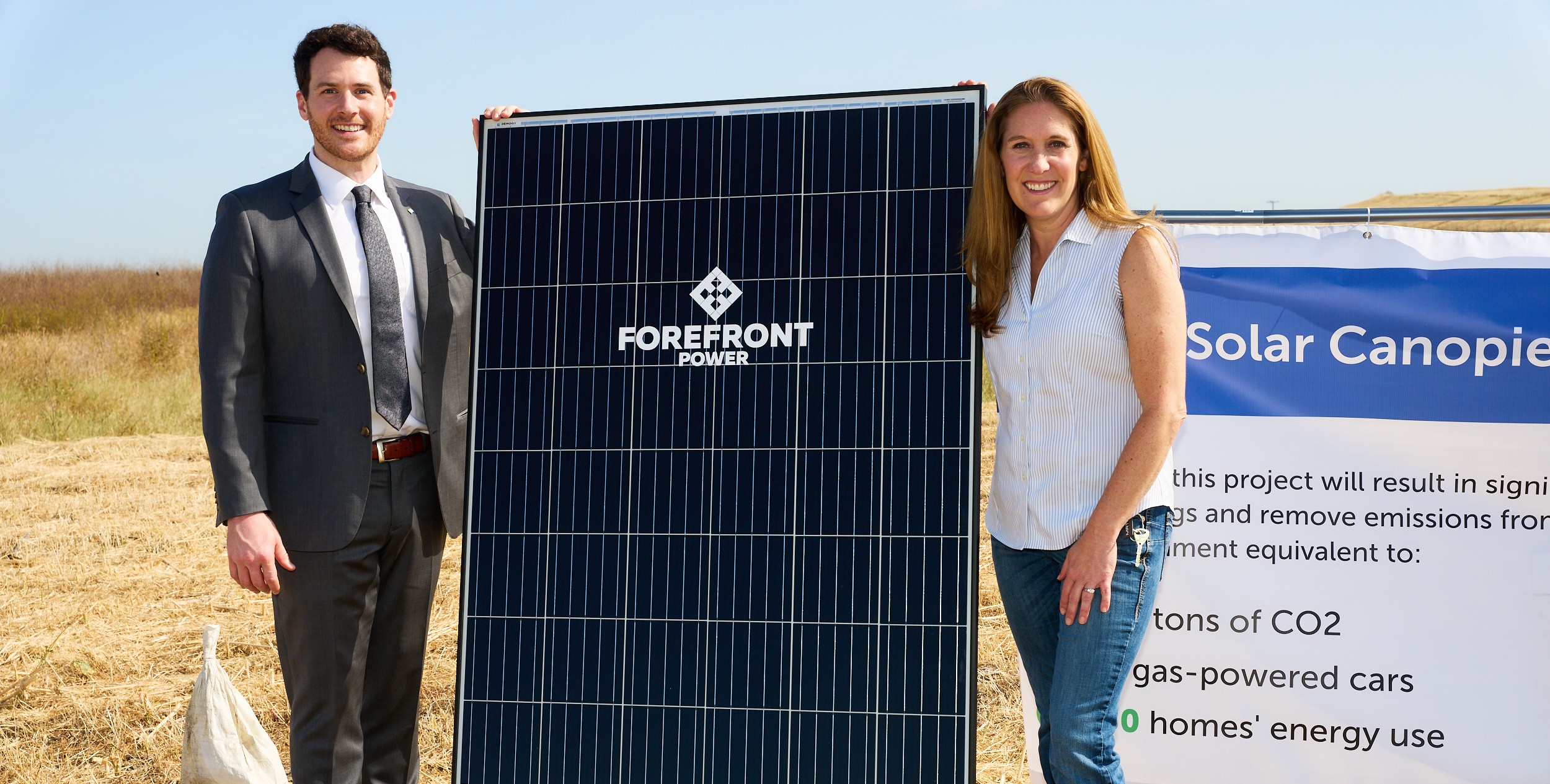 Man in suit and woman in casual clothes holding a Forefront Power solar panel outdoors.