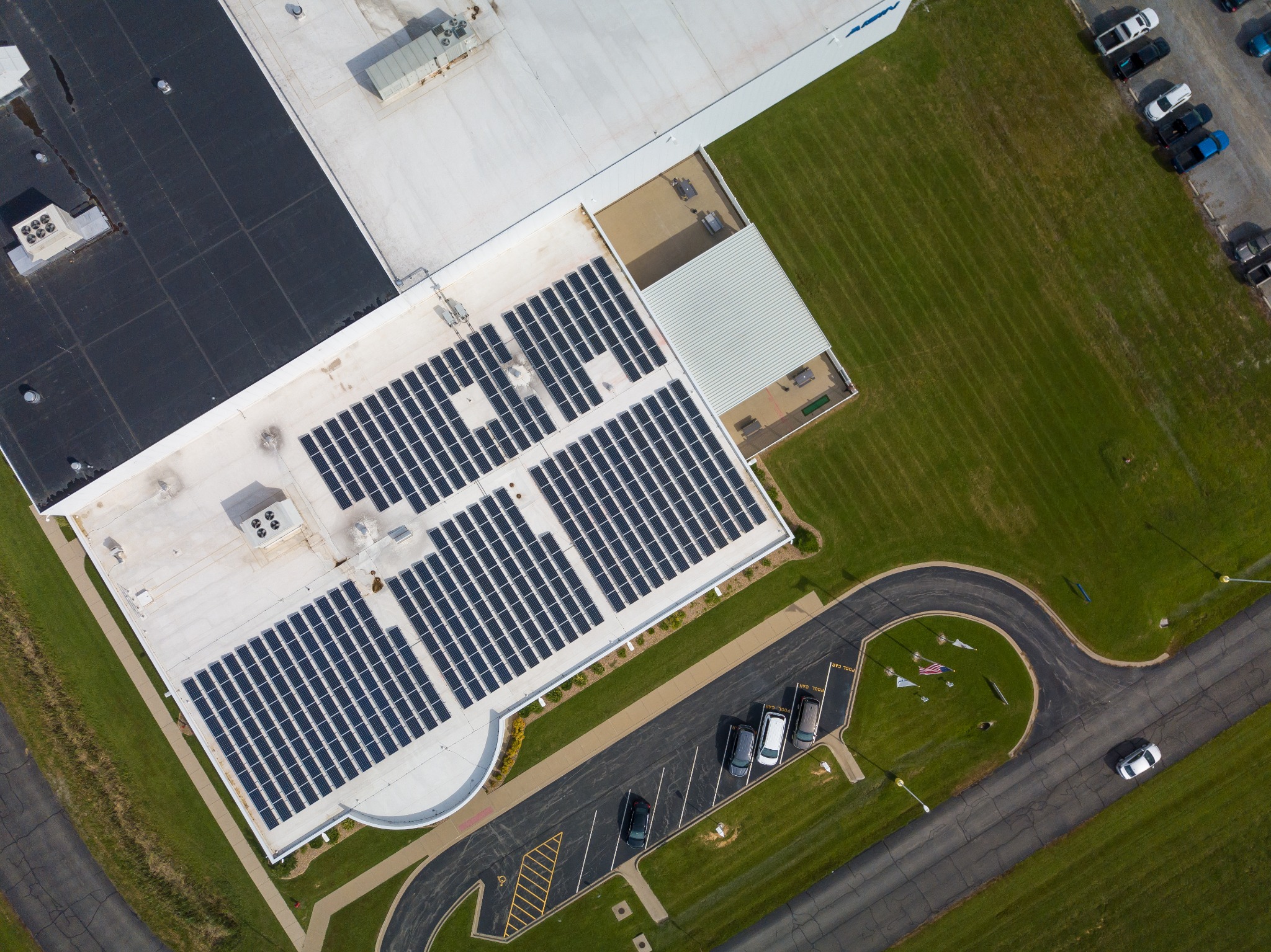 Aerial view of a building with solar panels on its roof and a parking lot with cars nearby.