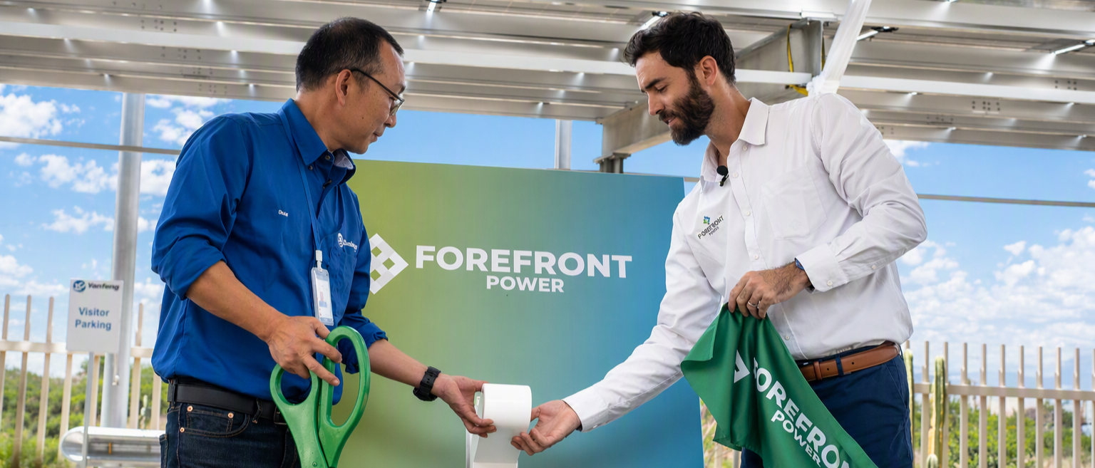 Two men in uniforms holding green scissors and a Forefront Power banner at an outdoor event.