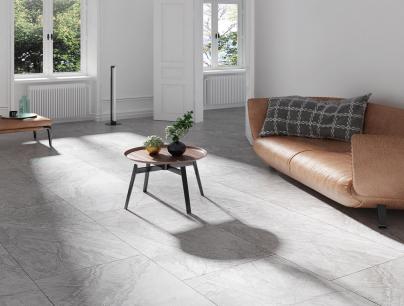 Minimalist living room with a brown leather sofa, a small round wooden coffee table with plants, and large windows letting in natural light.